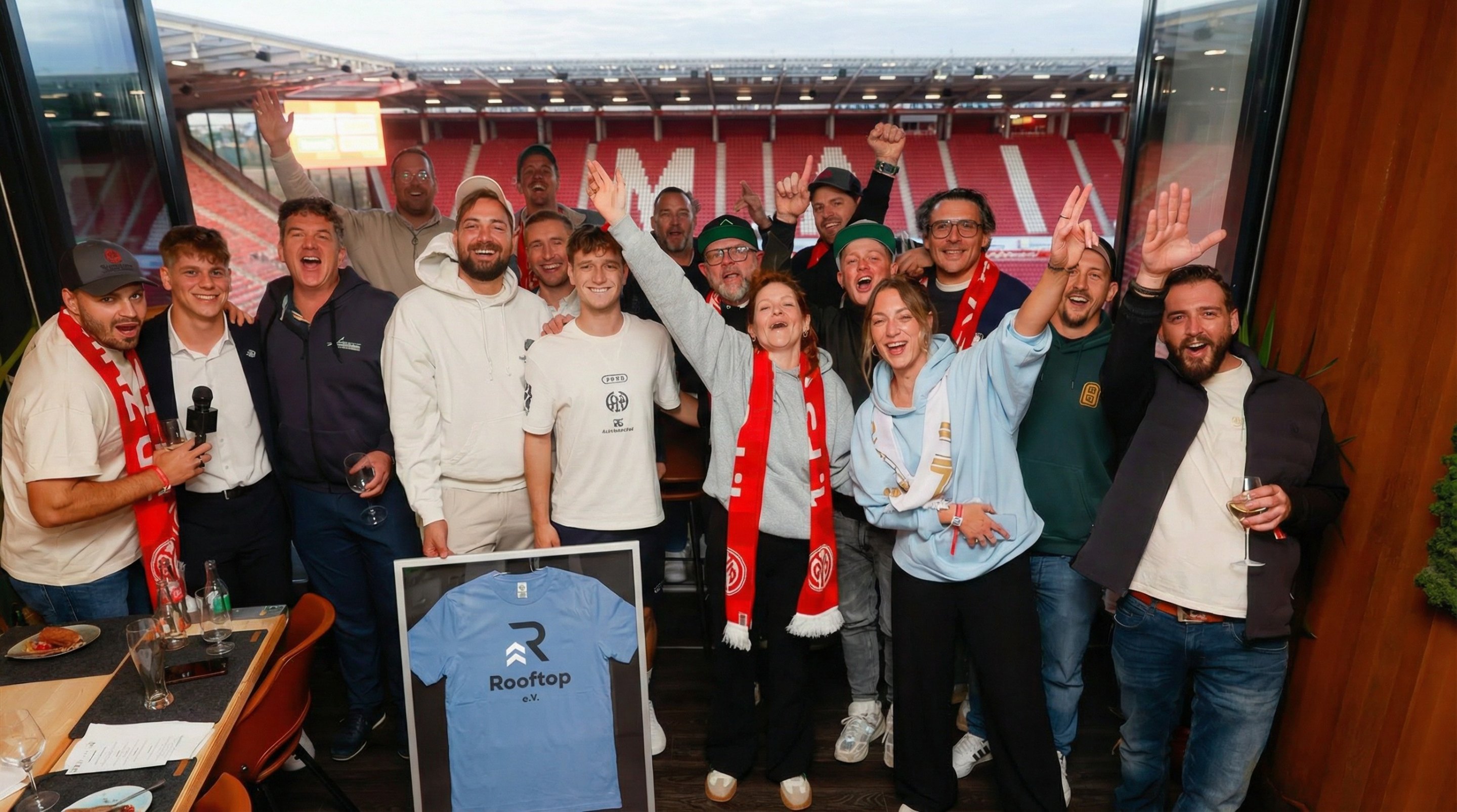 Gruppe von Rooftop-Mitgliedern, die gemeinsam ein gerahmtes Rooftop-Trikot präsentieren.